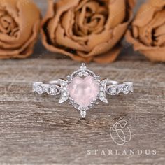 an engagement ring with a pink stone surrounded by white diamonds on a wooden table next to roses