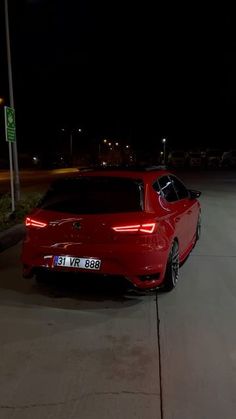 a red car parked on the side of a road at night with its lights on