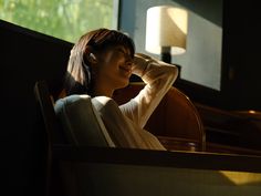 a woman sitting in a chair with her hand on her head and looking out the window