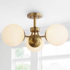 a ceiling light with three globes hanging from it's center point in front of a window