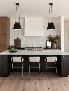 a kitchen with two black pendant lights hanging over the island and three white stools