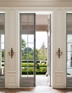 an open door leading to a garden with hedges in the back ground and large windows on either side