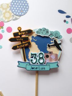 there is a cake topper that has an airplane and street signs on it with confetti in the background