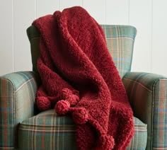 a red blanket sitting on top of a green chair next to a plaid pillow and arm chair