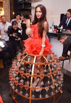 a woman in a red dress standing next to a wine rack filled with champagne glasses