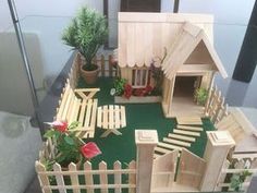 a model of a house made out of wood and fake flowers on the ground in front of it