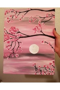 a person is holding up a painting with pink flowers and the moon in the background