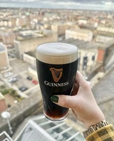 a person holding up a guinness glass in front of a cityscape