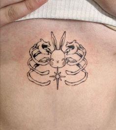 a woman's back with a tattoo on her stomach that has two cats and a cross in the middle