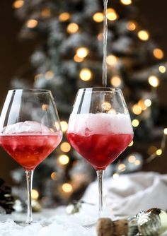 two wine glasses filled with red and pink liquid sitting in front of a christmas tree