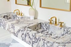 two marble sinks with gold faucets in a white and black bathroom area next to mirrors