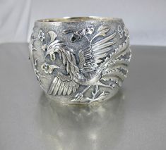 Fabulous beautifully detailed antique Qing Dynasty Chinese wide Sterling Silver bangle Bracelet with raised image of a Phoenix and a Dragon with what looks like the Sun at the center.  According to the hallmark CHINA 100 23 this piece is mid19th century and may have been one of a pair of Wedding Bracelets.  The Dragon represents the Masculine with its strength and power, while the Phoenix embodies the feminine, representing grace and beauty.  Together they signify the harmonious union of opposites. A stunning piece that will become a family heirloom for many years to come. A wonderful addition to your antique jewelry collection! Bracelet is in great condition. Opens and closes securely.  Hallmarked CHINA 100 23. Measures 2.25 inches from top to bottom and the inside measures 6.50 inches ar Victorian Cuff Bracelet With Intricate Design For Ceremonial Occasions, Victorian Cuff Bracelet With Intricate Design For Ceremonial, Victorian Style Ceremonial Cuff Bracelet With Intricate Design, Victorian Bangle With Intricate Design For Ceremonial Occasions, Antique Etched Bangle For Wedding, Antique Etched Wedding Bangle, Antique Engraved Wide Band Jewelry, Antique Wide Band Engraved Jewelry, Victorian Ceremonial Cuff Bracelet Bangle