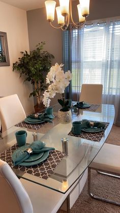 a dining room table is set with place settings and flowers in vases on the glass top