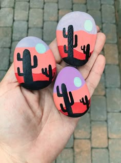 three painted rocks in the shape of cacti on a brick walkway, one is holding