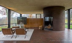 an open room with chairs and a fireplace in the center, surrounded by glass walls