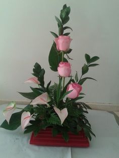 pink roses and greenery in a red vase on a white tableclothed surface