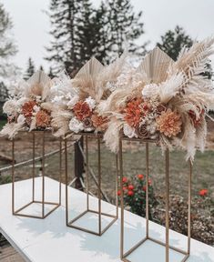 three gold vases with flowers and feathers in them sitting on a white table outside