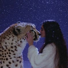 a woman kissing a cheetah on the nose in front of a snow covered sky