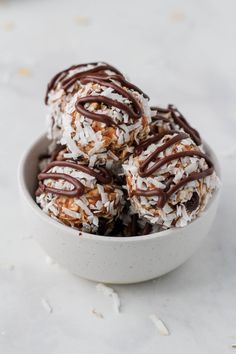 chocolate covered coconut balls in a bowl on a white table top with shredded coconut and drizzled dark chocolate