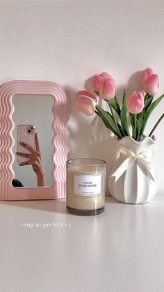 a vase with flowers and a candle on a table next to a mirror that says one so perfect