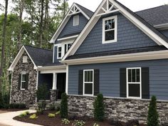 a blue house with white trim and stone accents in the front yard, surrounded by trees