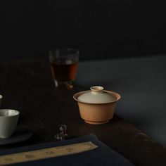 a table topped with cups and saucers on top of a wooden table next to a book