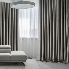 a white couch sitting in front of a window next to a curtained wall with drapes