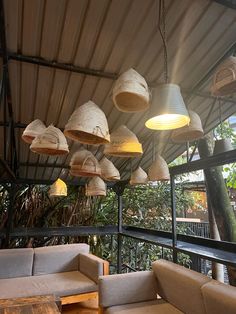 several lamps hanging from the ceiling above couches and tables in an outdoor area with wood flooring