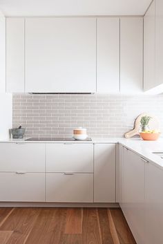 a kitchen with white cabinets and wood flooring is pictured in this image, there are two bowls on the counter