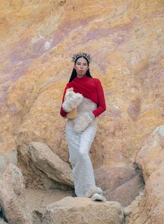 a woman standing on top of a rock next to a white teddy bear wearing a crown