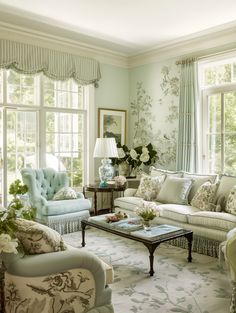 a living room filled with lots of furniture next to two large windows covered in curtains