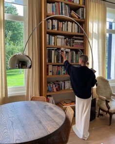 a woman standing in front of a bookshelf with a lamp on top of it