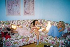 two women sitting on a floral couch in a living room with blue walls and pink flowers