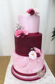 a three tiered cake with pink and purple frosting on the top, decorated with flowers