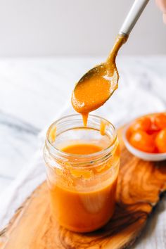 a spoon full of sauce being lifted from a jar with tomatoes in the bowl behind it