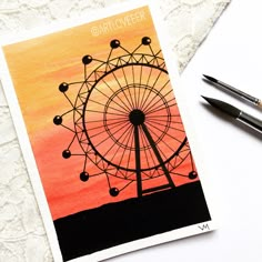 a card with an image of a ferris wheel on it and two pens next to it