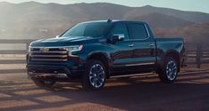 a black truck is parked in front of a wooden fence and mountain range behind it