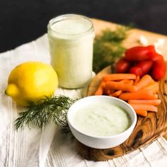 a wooden cutting board topped with carrots next to a bowl of dip