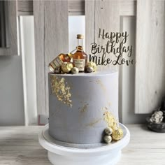 a birthday cake decorated with gold and silver icing, topped with an assortment of liquor bottles