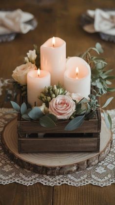 three white candles are sitting on top of a wooden box with flowers and greenery