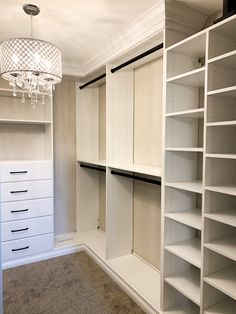 an empty walk - in closet with white shelving and chandelier hanging from the ceiling