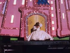 a woman in a white dress sitting on top of a stage with lights all around her