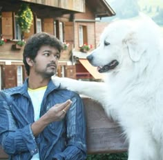 a man sitting on a bench next to a white dog and holding his hand out