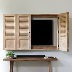 an entertainment center with wooden shutters and a tv on top of it, in front of a white wall