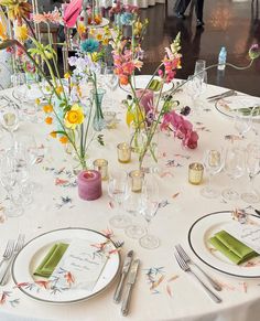 a table set with place settings and flowers in vases on the centerpiece, along with napkins