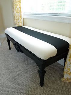 a black and white bench in front of a window with yellow drapes on it