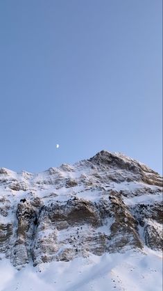 a mountain covered in snow under a blue sky with a half moon visible above it