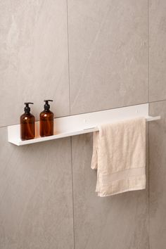 two brown bottles are sitting on a white shelf in the bathroom next to a towel and soap dispenser