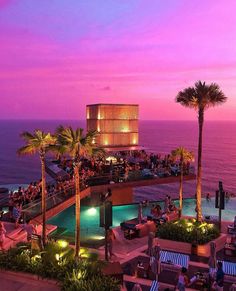 people are sitting at tables near the pool in front of an ocean and palm trees