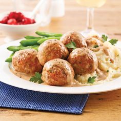 meatballs and mashed potatoes on a white plate with green beans next to a glass of wine